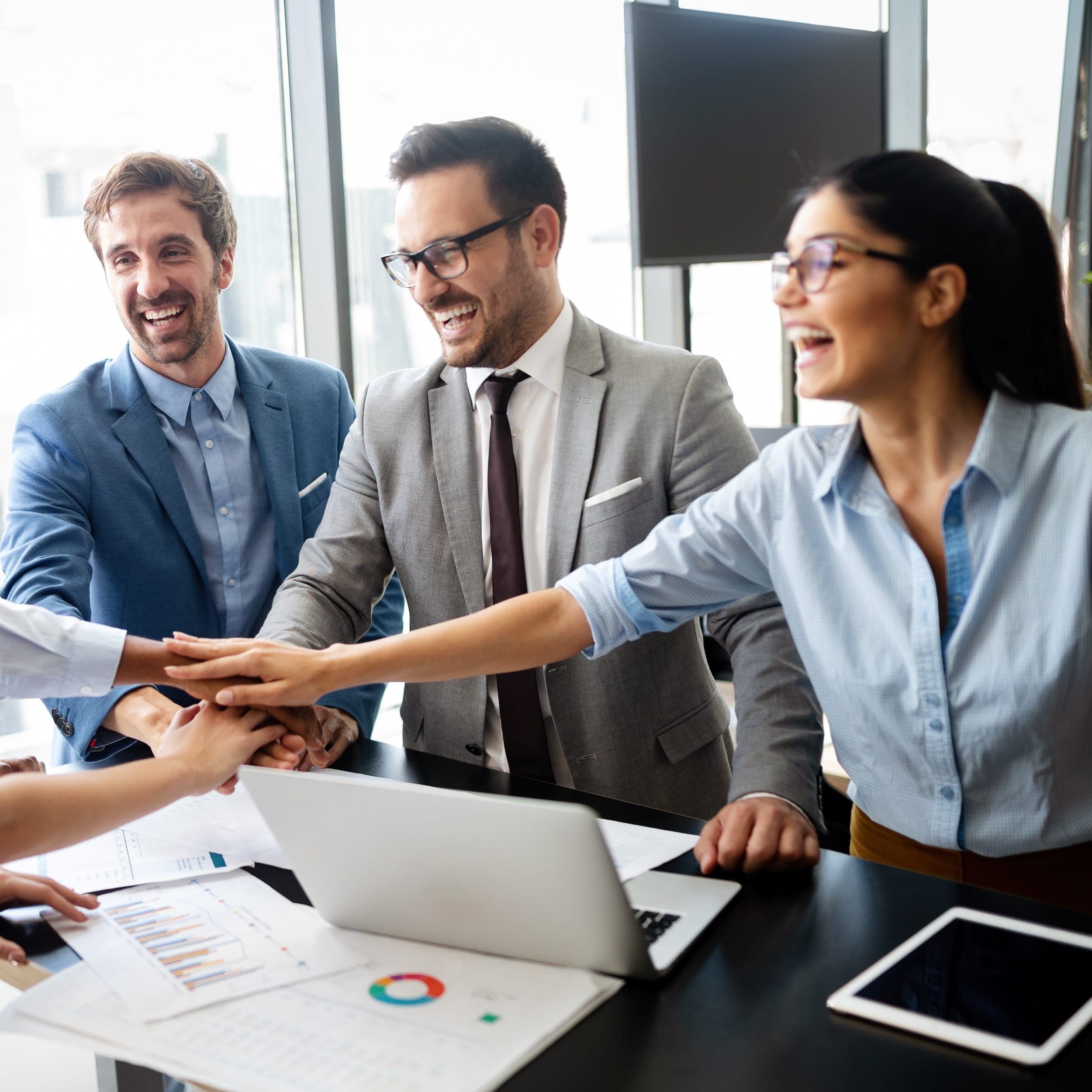 Ein fröhliches Team legt im Büro die Hände zusammen und zeigt Zusammenhalt und Motivation bei der gemeinsamen Arbeit. Ein fröhliches Team legt im Büro die Hände zusammen und zeigt Zusammenhalt und Motivation bei der gemeinsamen Arbeit.