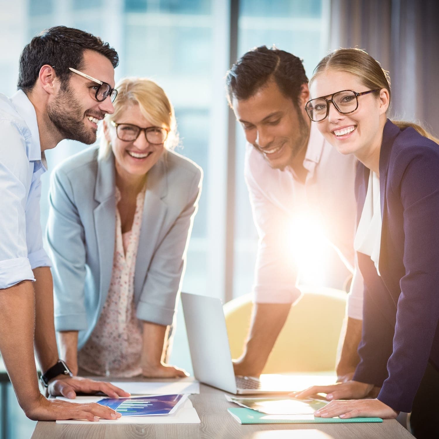 Vier Geschäftspersonen stehen lächelnd an einem Konferenztisch und besprechen gemeinsam Strategien – Symbol für erfolgreiche Teamarbeit und Zusammenarbeit. Vier Geschäftspersonen stehen lächelnd an einem Konferenztisch und besprechen gemeinsam Strategien – Symbol für erfolgreiche Teamarbeit und Zusammenarbeit.